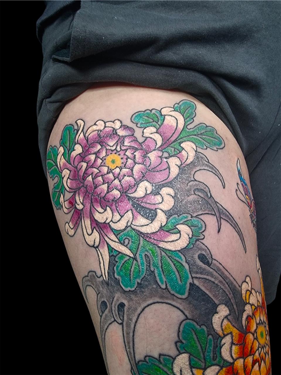 Tatuagem japonesa de crisântemo roxo e folhas verdes na coxa