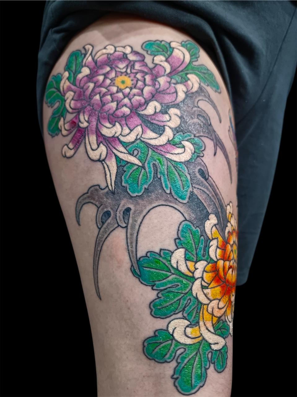 Detalhe de tatuagem japonesa com crisântemos roxos, amarelos e folhas verdes